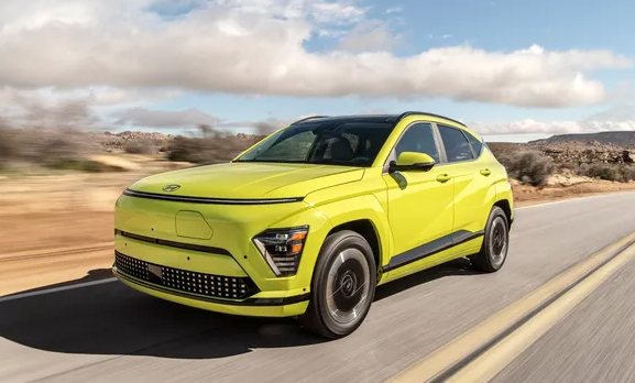 bright yellow electric SUV driving on an empty desert road under a blue sky with scattered clouds