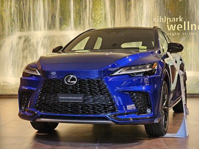 front view of a blue Lexus car displayed indoors with a waterfall background and a signboard next to the vehicle