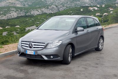 gray Mercedes-Benz compact hatchback car parked on a road with greenery and hills in the background