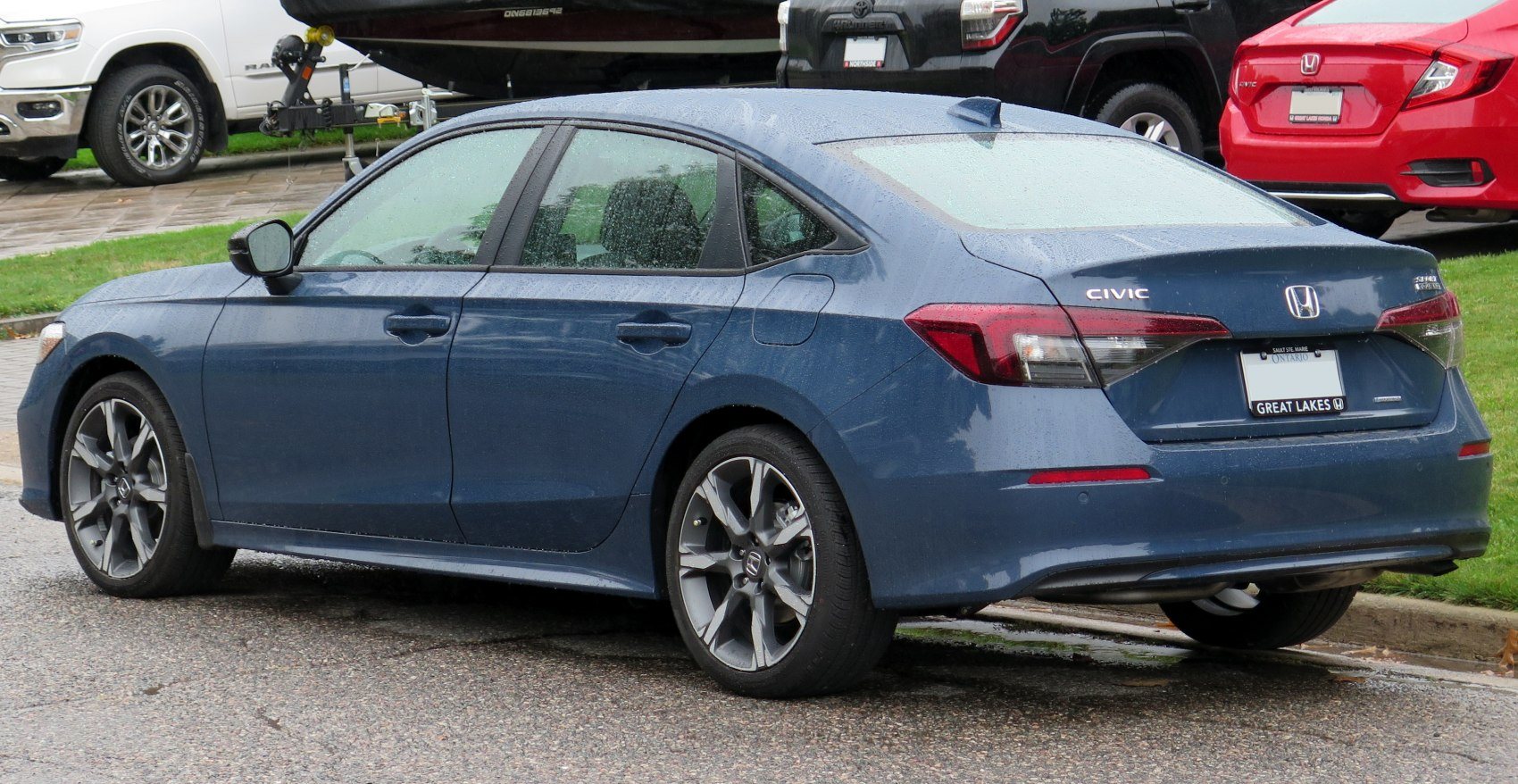blue Honda Civic sedan parked on street showing side and rear view with rain droplets on car body