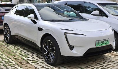 White modern electric SUV parked beside other vehicles on a paved surface with green license plate