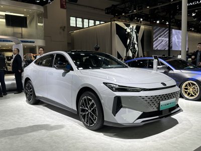 white modern sedan car displayed at an auto show with sleek design and black alloy wheels under bright showroom lighting