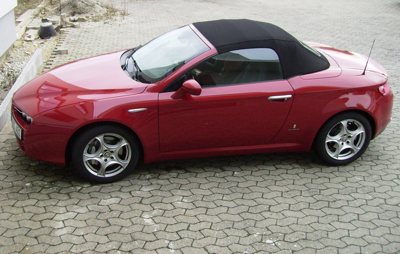 side view of a red convertible sports car with a black soft top roof parked on a paved surface