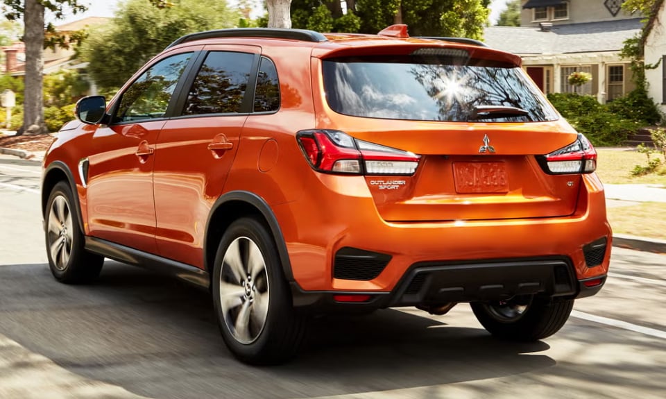 Orange Mitsubishi Outlander Sport SUV driving on a residential street with houses and trees in the background