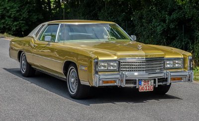 gold vintage Cadillac Eldorado car parked on road with trees in background