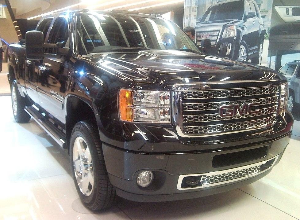 front and side view of a black GMC pickup truck displayed indoors with shiny chrome grille and headlights