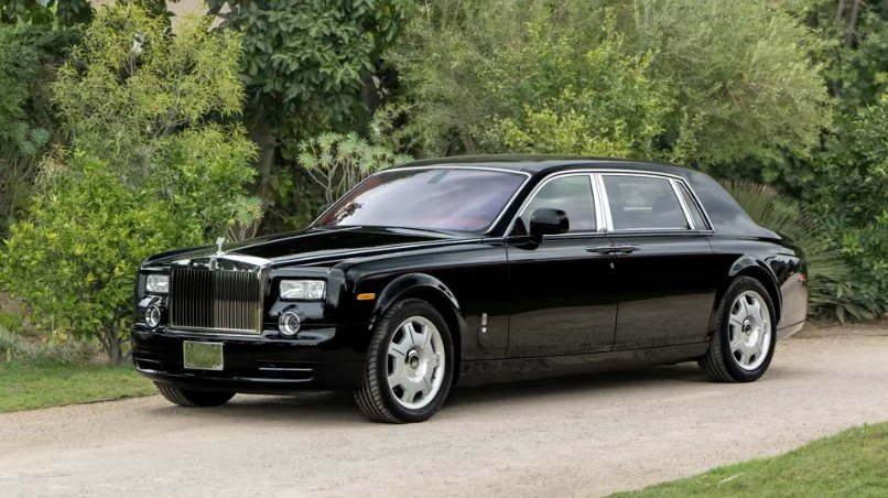black luxury sedan parked on a dirt road with green trees and bushes in the background