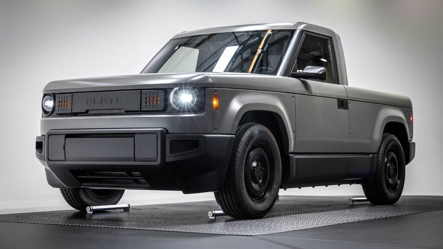 front three-quarter view of a matte gray electric pickup truck with modern LED headlights and a minimalist design on a studio backdrop