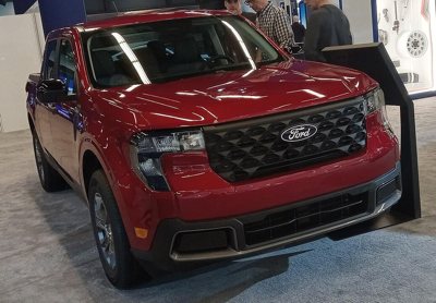 front view of a red Ford pickup truck displayed indoors with people in the background