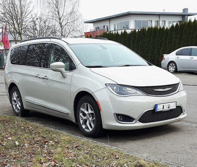 white Chrysler Pacifica minivan parked on a street near a grassy curb with houses and trees in the background