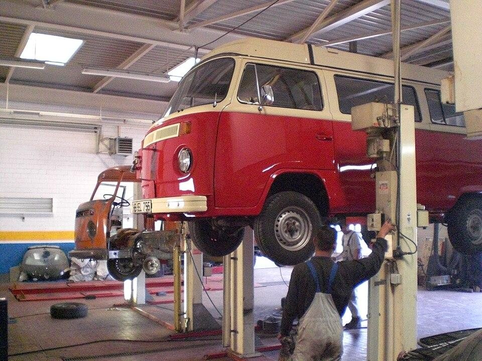 red vintage van elevated on a hydraulic car lift in an auto repair garage with mechanics working nearby