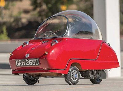small red microcar with a bubble-shaped transparent roof and three wheels parked outdoors