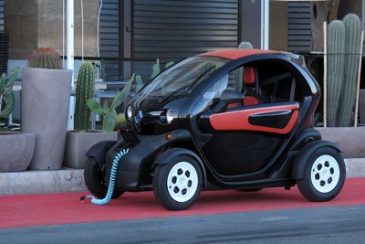 Small black and red electric compact car charging on a red carpet next to potted cactus plants