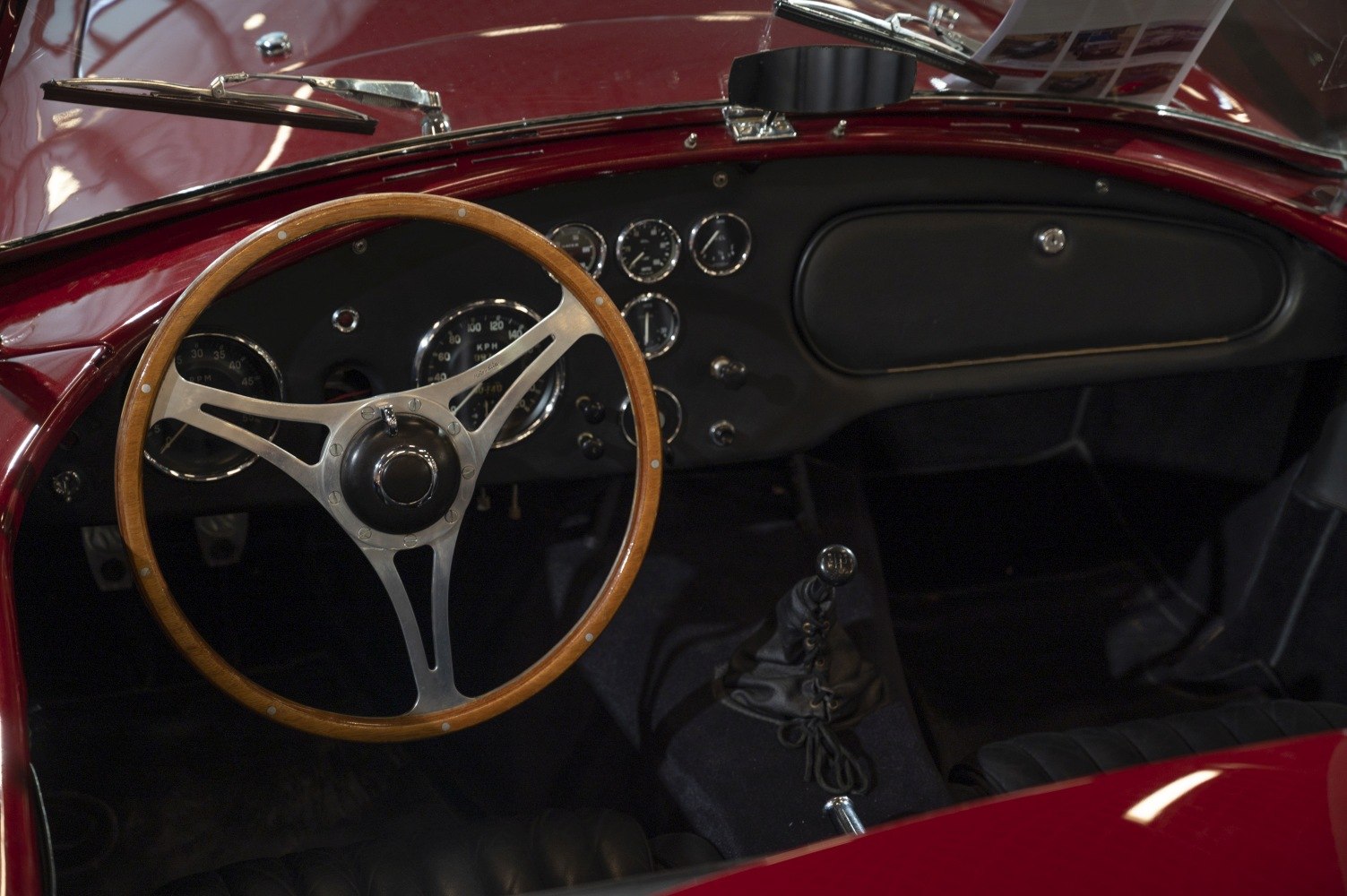 Wooden steering wheel with metal spokes and vintage analog dashboard.