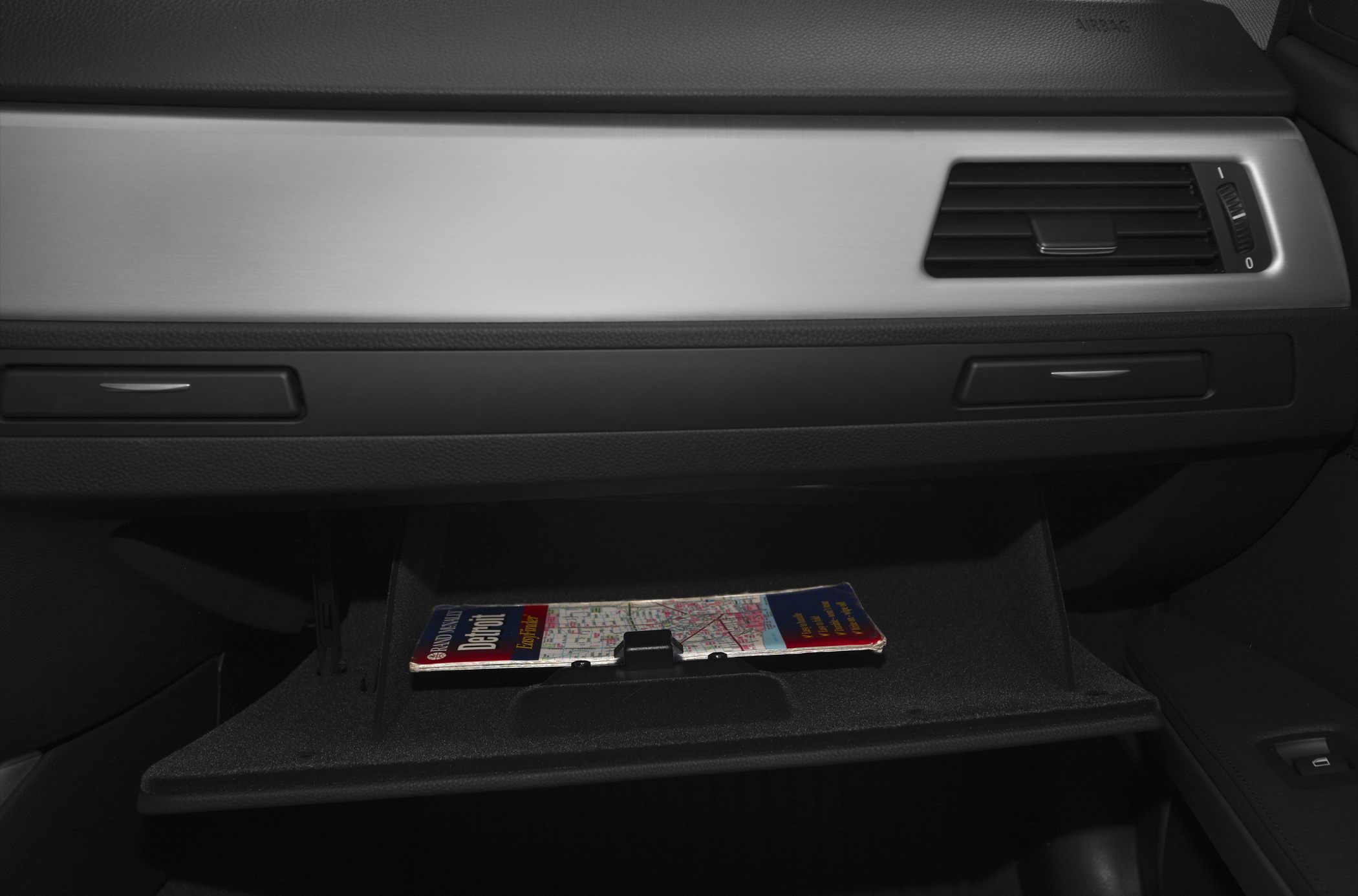 Open glove compartment with map inside and dashboard air vent