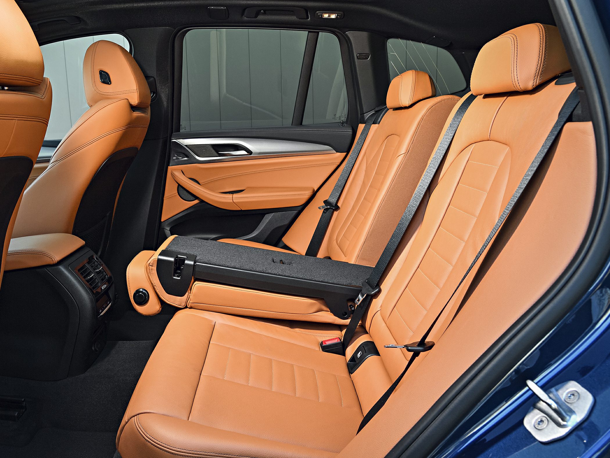 Tan leather rear seats with foldable center armrest and black seat belts.