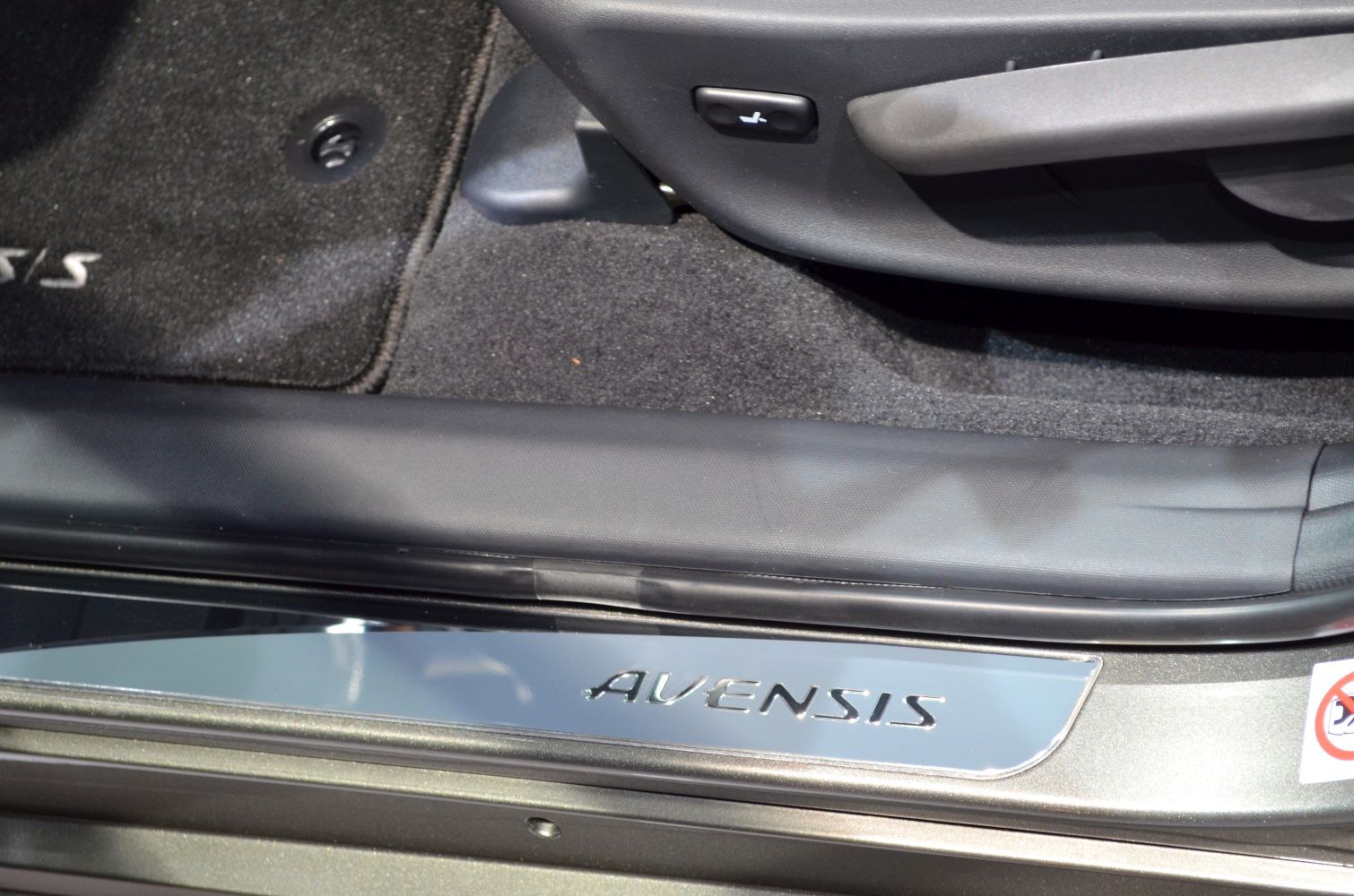 Close-up of car door sill with model nameplate and interior floor mat.