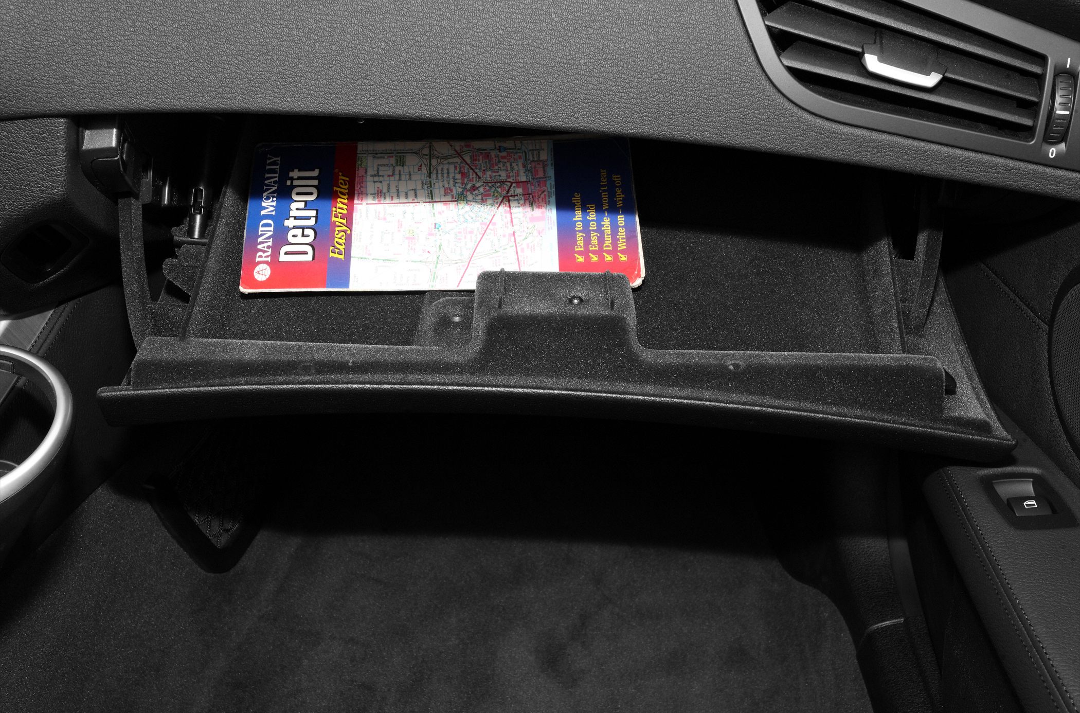 Open glove compartment with a map inside, black dashboard interior
