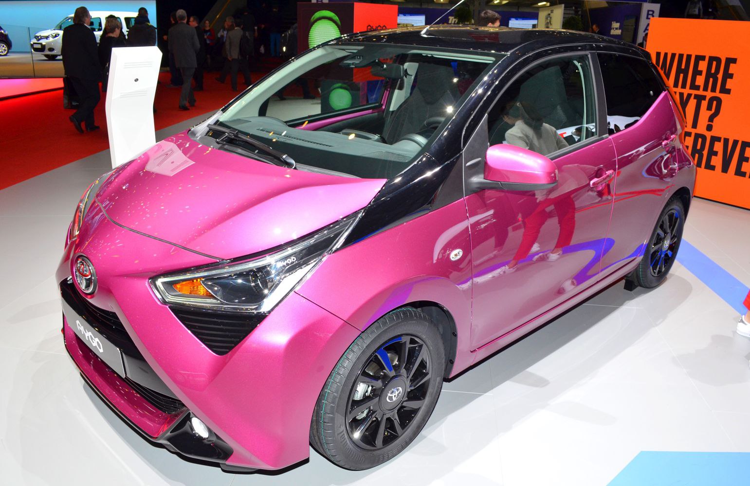 Front side view of a pink and black small hatchback with black alloy wheels.