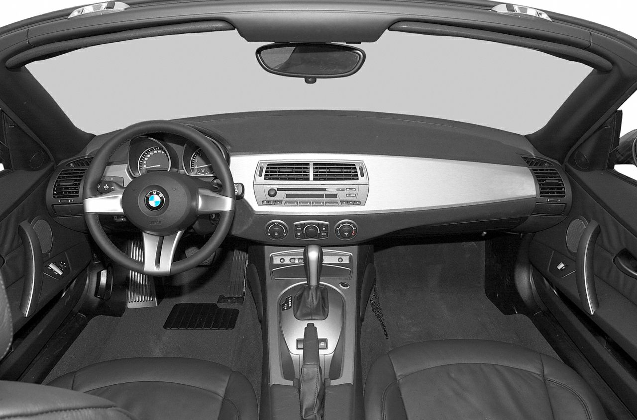 Steering wheel, dashboard, center console controls, and seating inside sporty convertible.