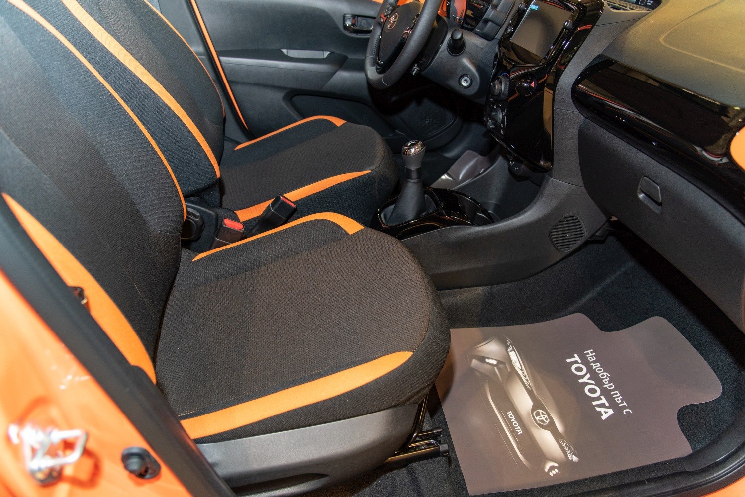 Sporty seats with orange accents and manual gearshift in a compact economy car interior.