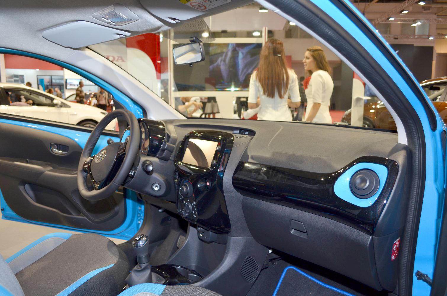 Compact car interior with manual gear lever, steering wheel, and central dashboard display.