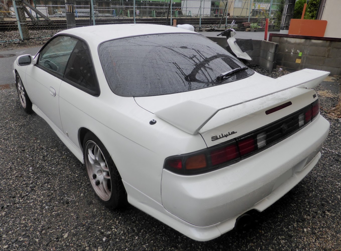 White coupe rear with spoiler and tail lights in rainy setting