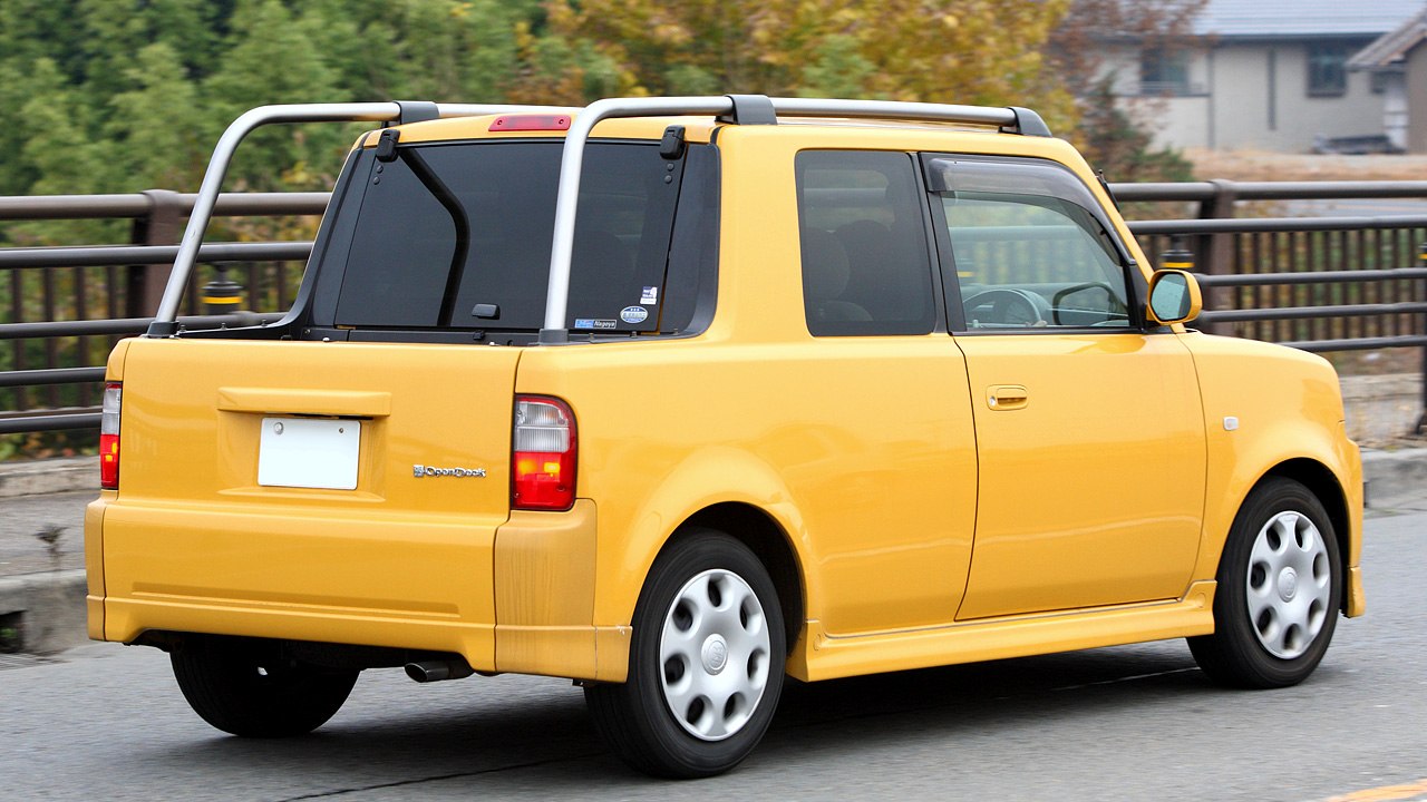 Rear-side view of a yellow compact utility vehicle with open cargo deck and roll bars