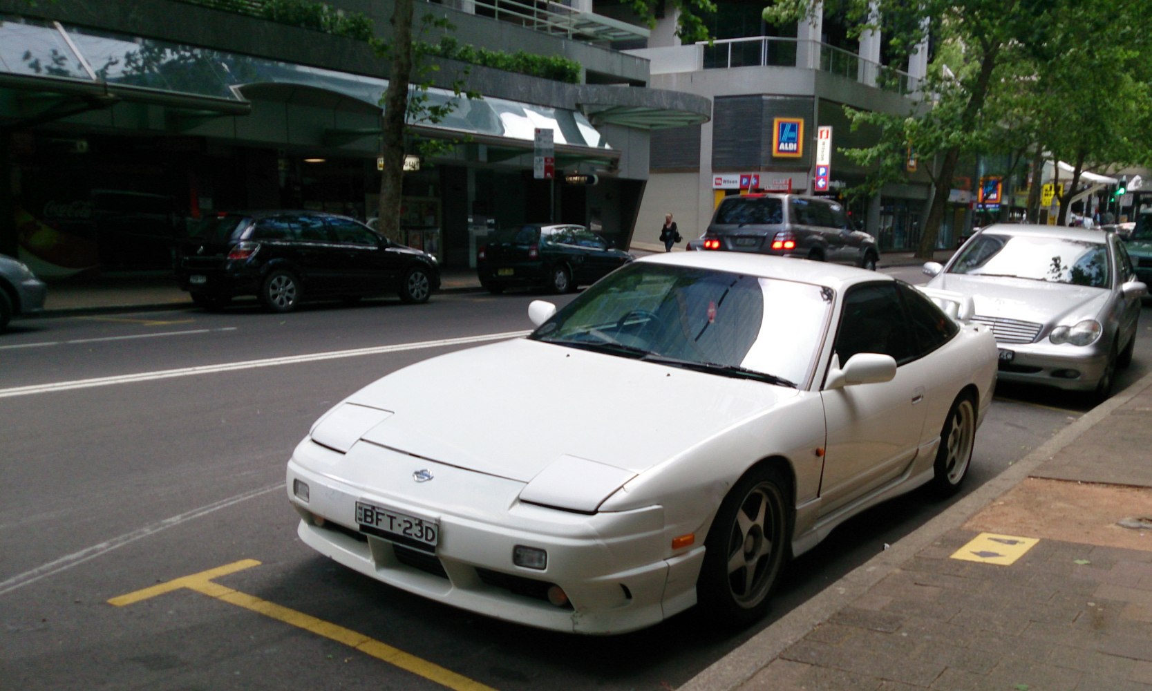 White coupe with pop-up headlights and sporty wheels parked on street