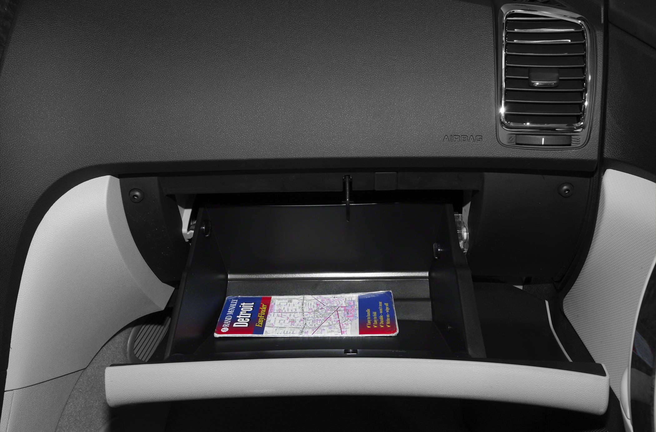 Open glove box with a map inside featuring dashboard air vent and airbag.