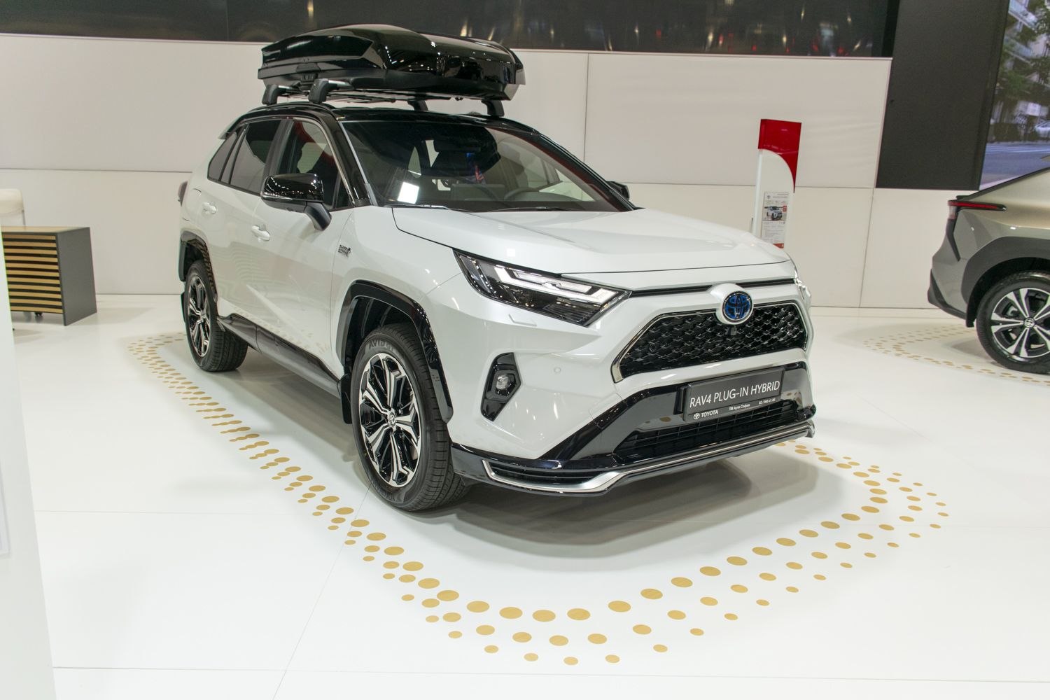 Front-side view of white SUV with roof box on display