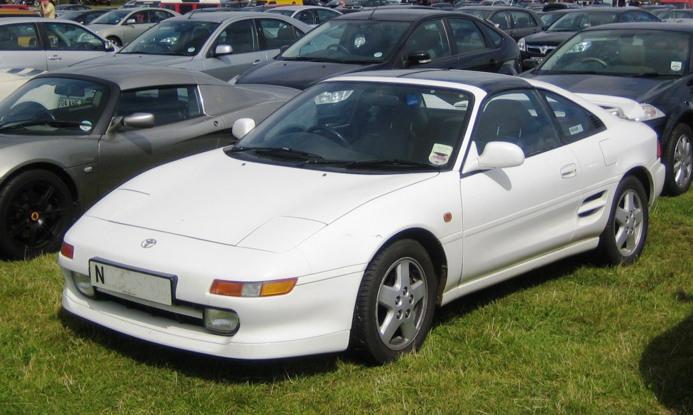White mid-engine sports coupe with pop-up headlights and alloy wheels.