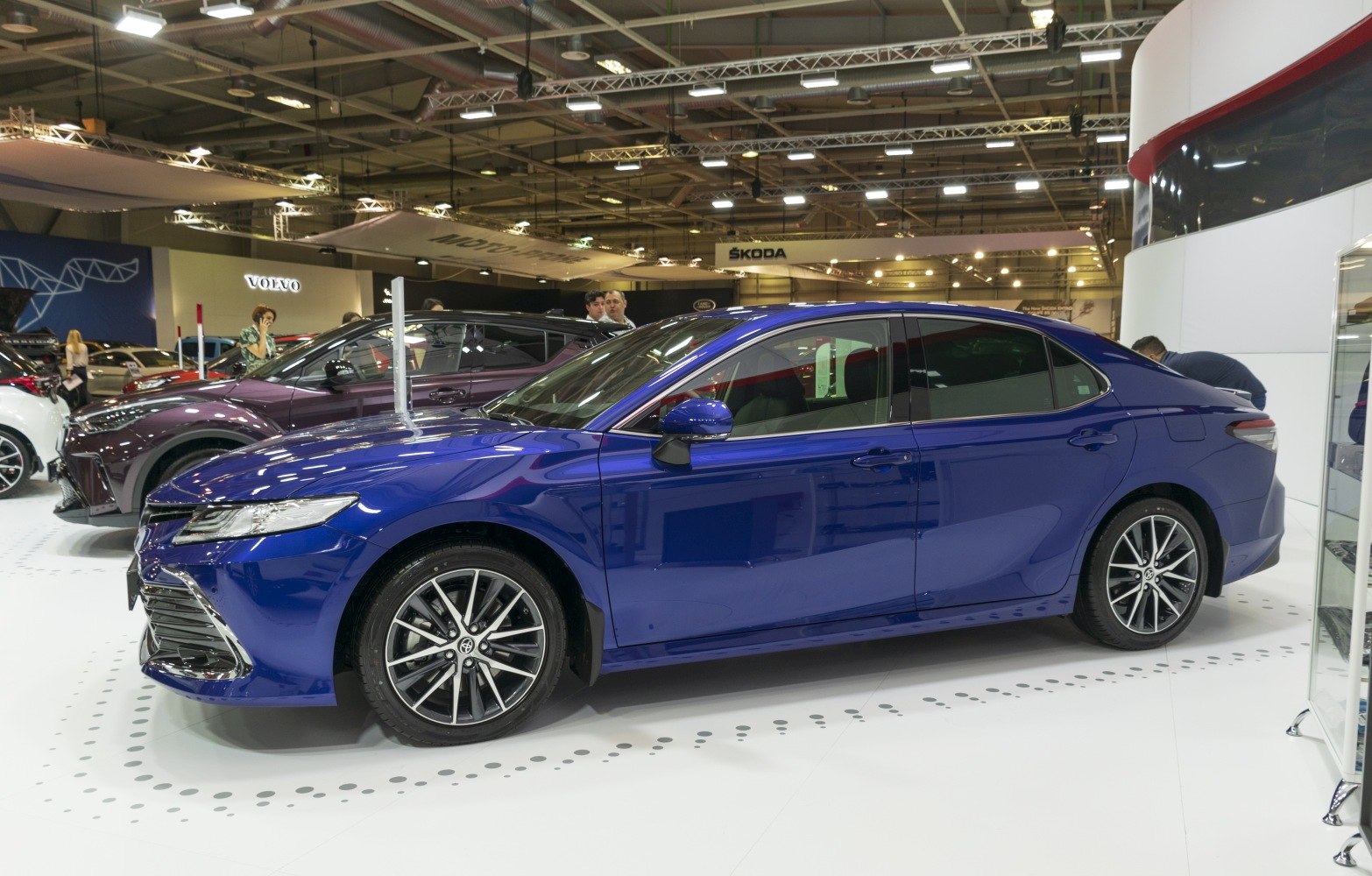 Blue sedan side profile with alloy wheels under indoor show lighting