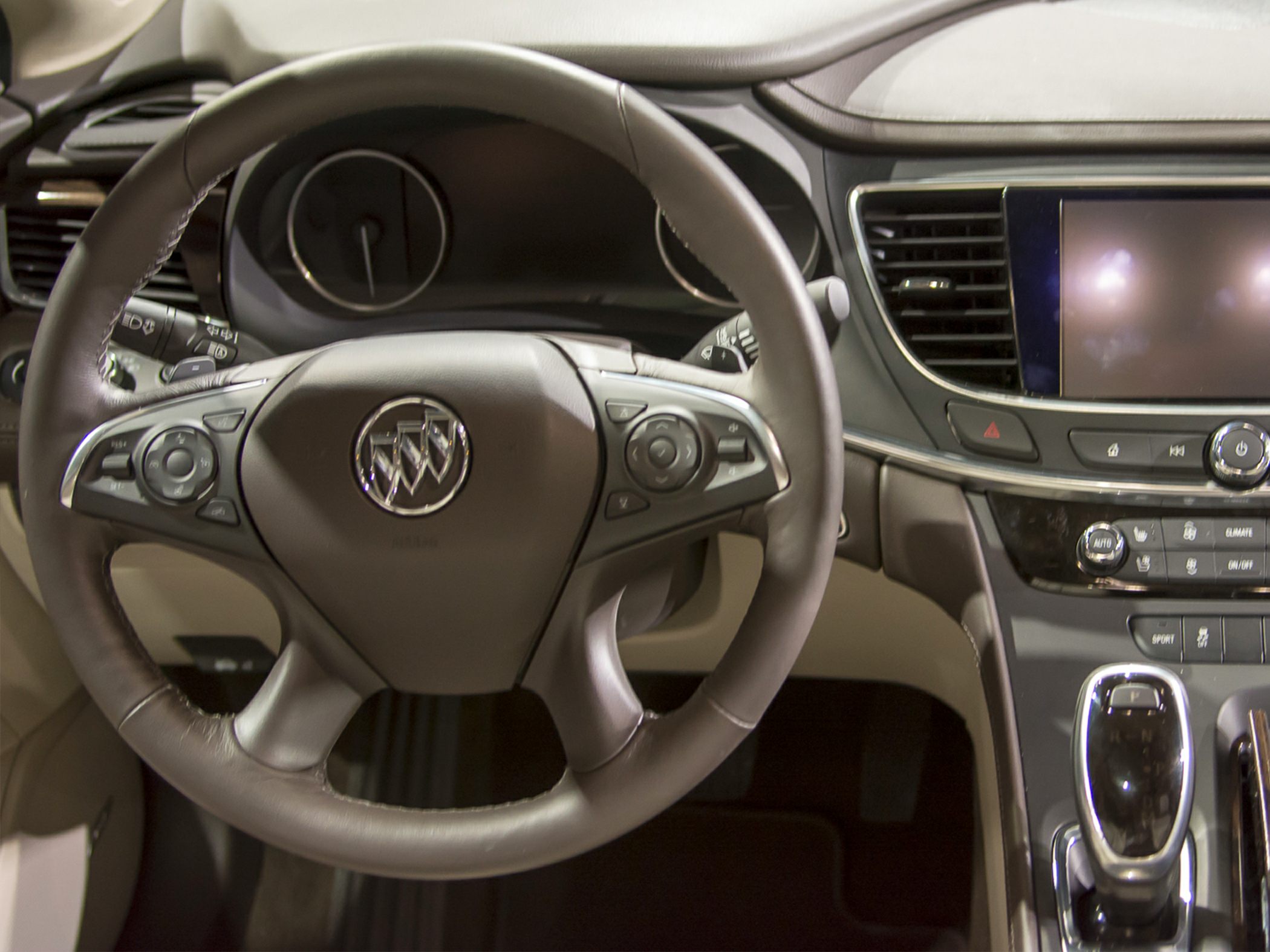 Steering wheel with emblem, dashboard, infotainment screen, and controls
