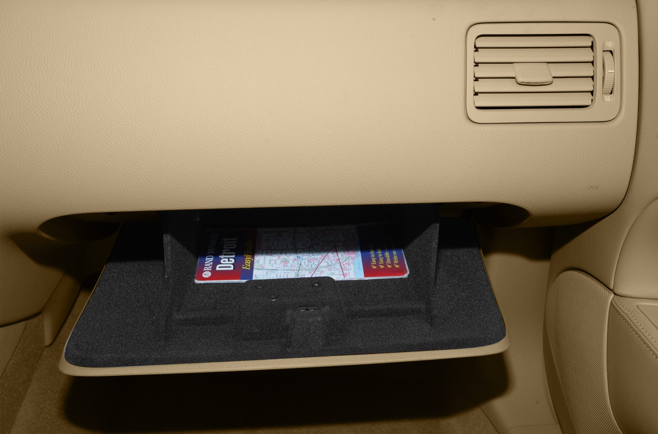 Open glove compartment and dashboard air vent inside beige car interior