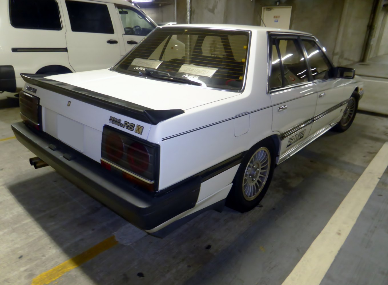 Vintage white sedan with rear spoiler, black trim, and distinct taillights