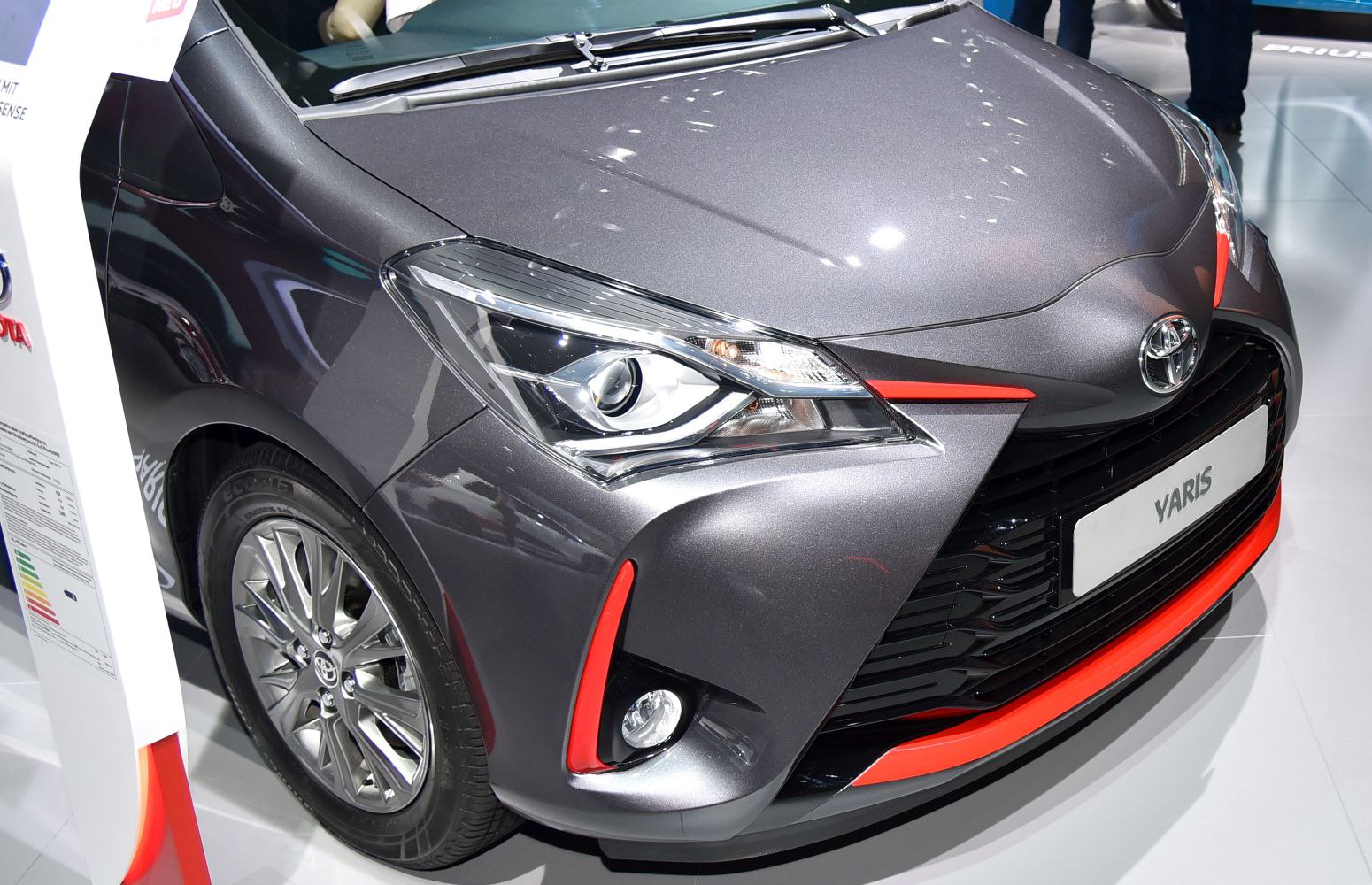 Close-up of front headlight, grille with red accents, and alloy wheel of a modern compact hatchback.