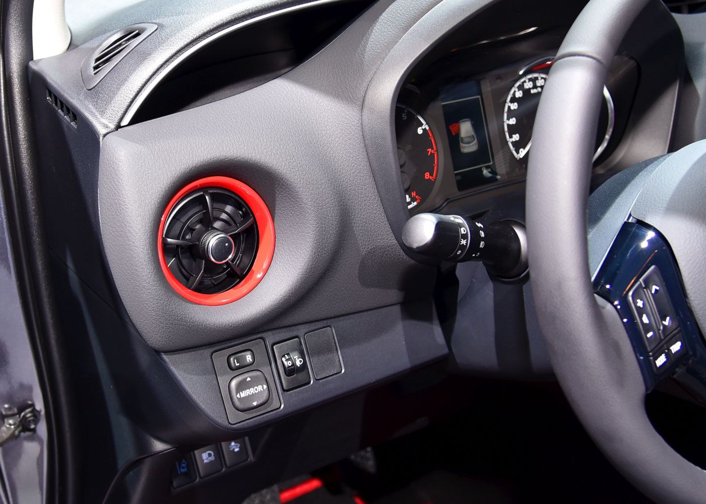 Circular air vent with red trim and adjacent dashboard controls