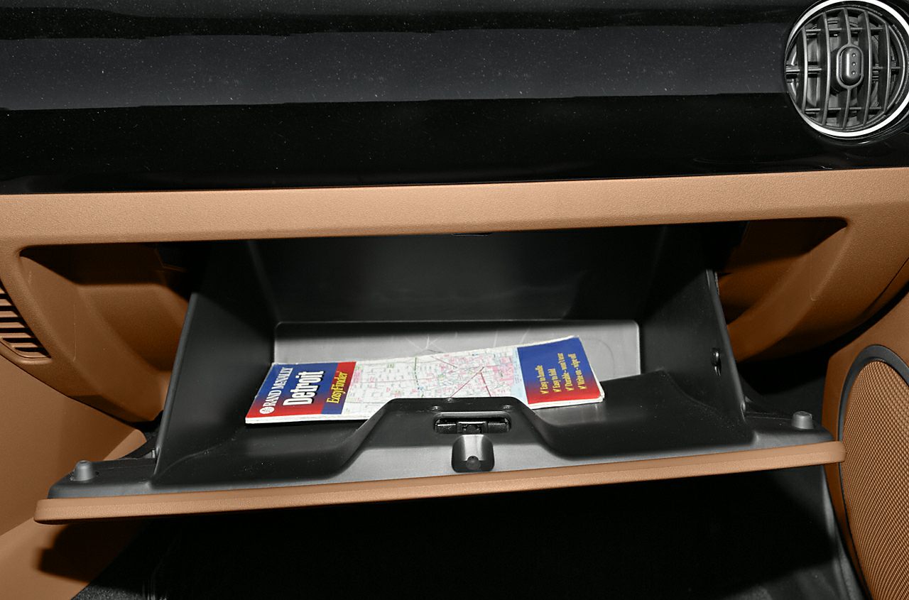 Open glove compartment with vintage road map inside, brown interior trim and air vent