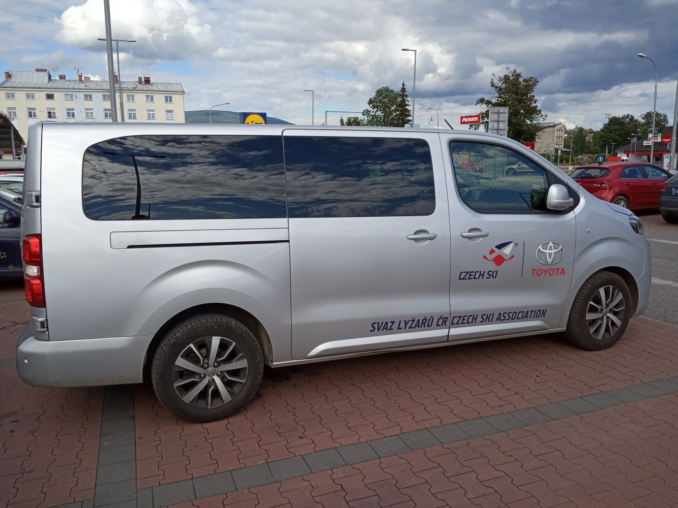 Side view of silver long wheelbase passenger van with tinted windows and promotional decals.