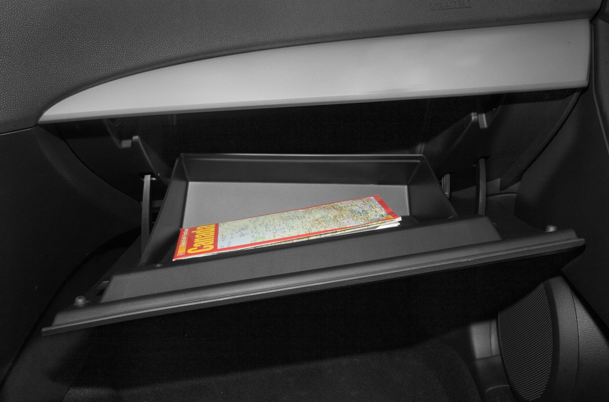 Open glove compartment with storage tray containing a folded map inside car interior