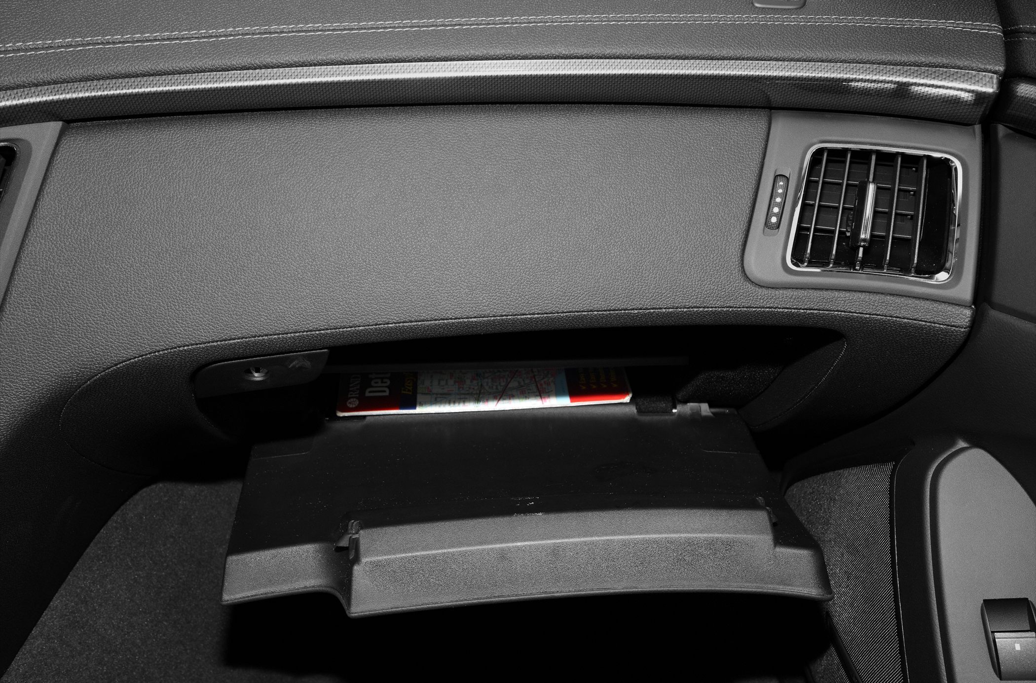 Glovebox open under dashboard with air vent and textured surface.