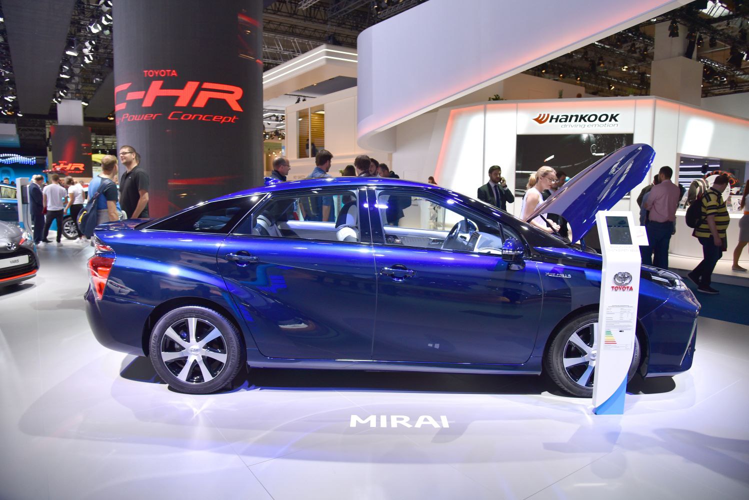 Side view of blue sedan with open hood at exhibition