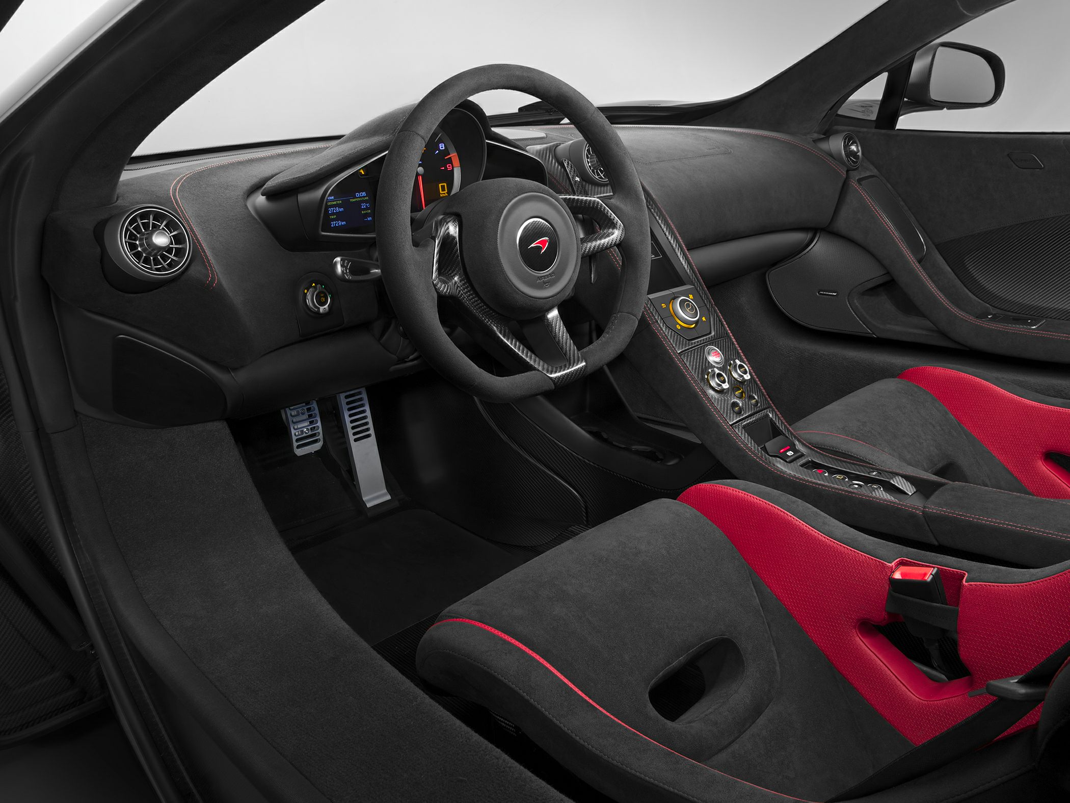 Carbon fiber steering wheel and red/black racing bucket seats inside a sports car.