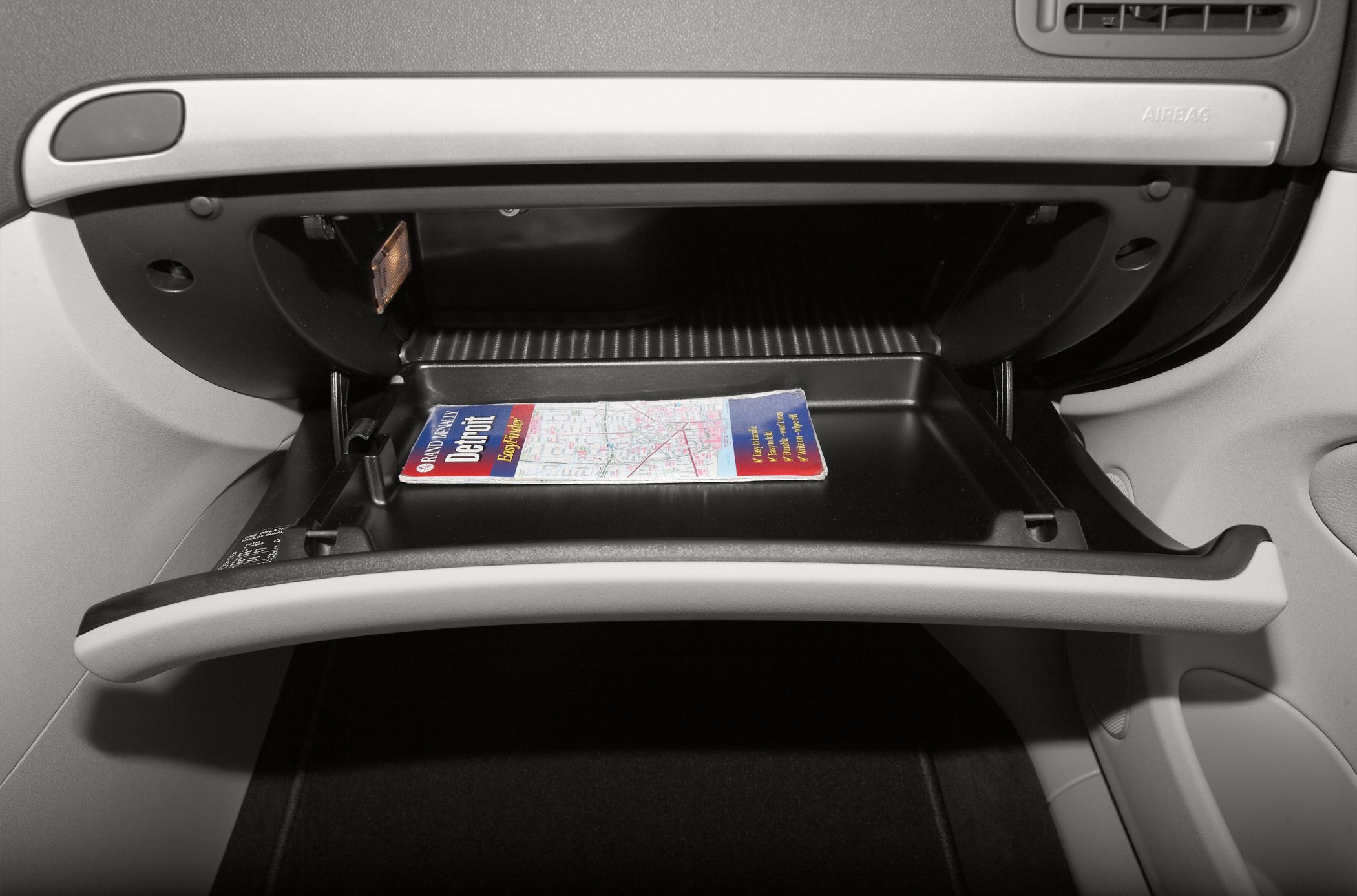 Car glovebox open with map inside, showing interior storage space and dashboard panel.