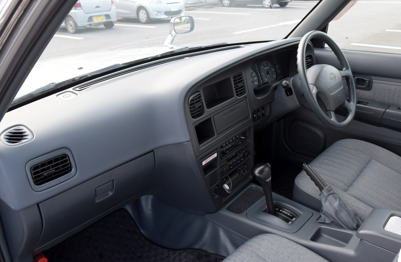 Dashboard, steering wheel, center console with gear shift and handbrake inside car interior.