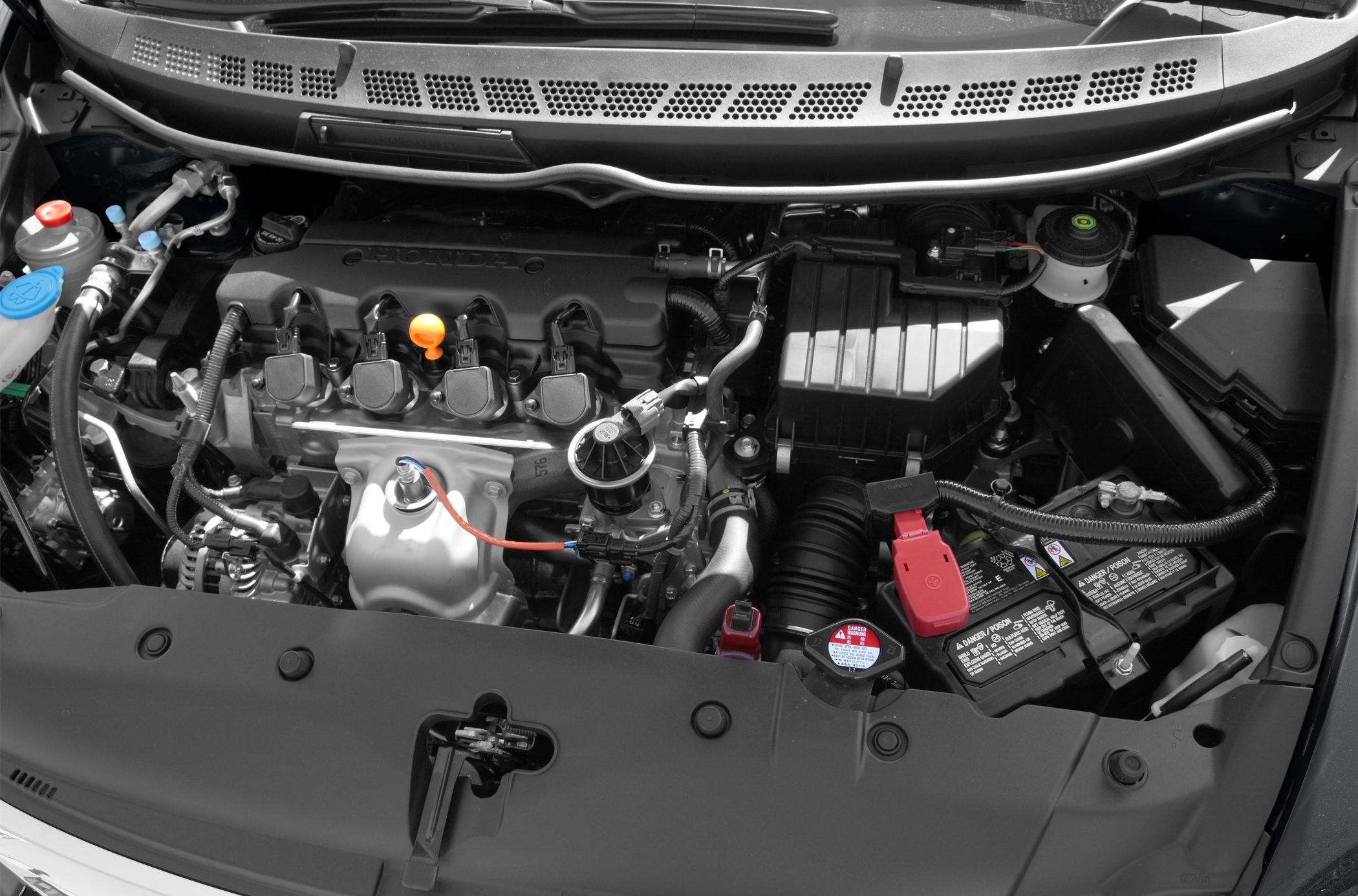 Close-up of ignition coils, battery, and fluid reservoirs in engine bay
