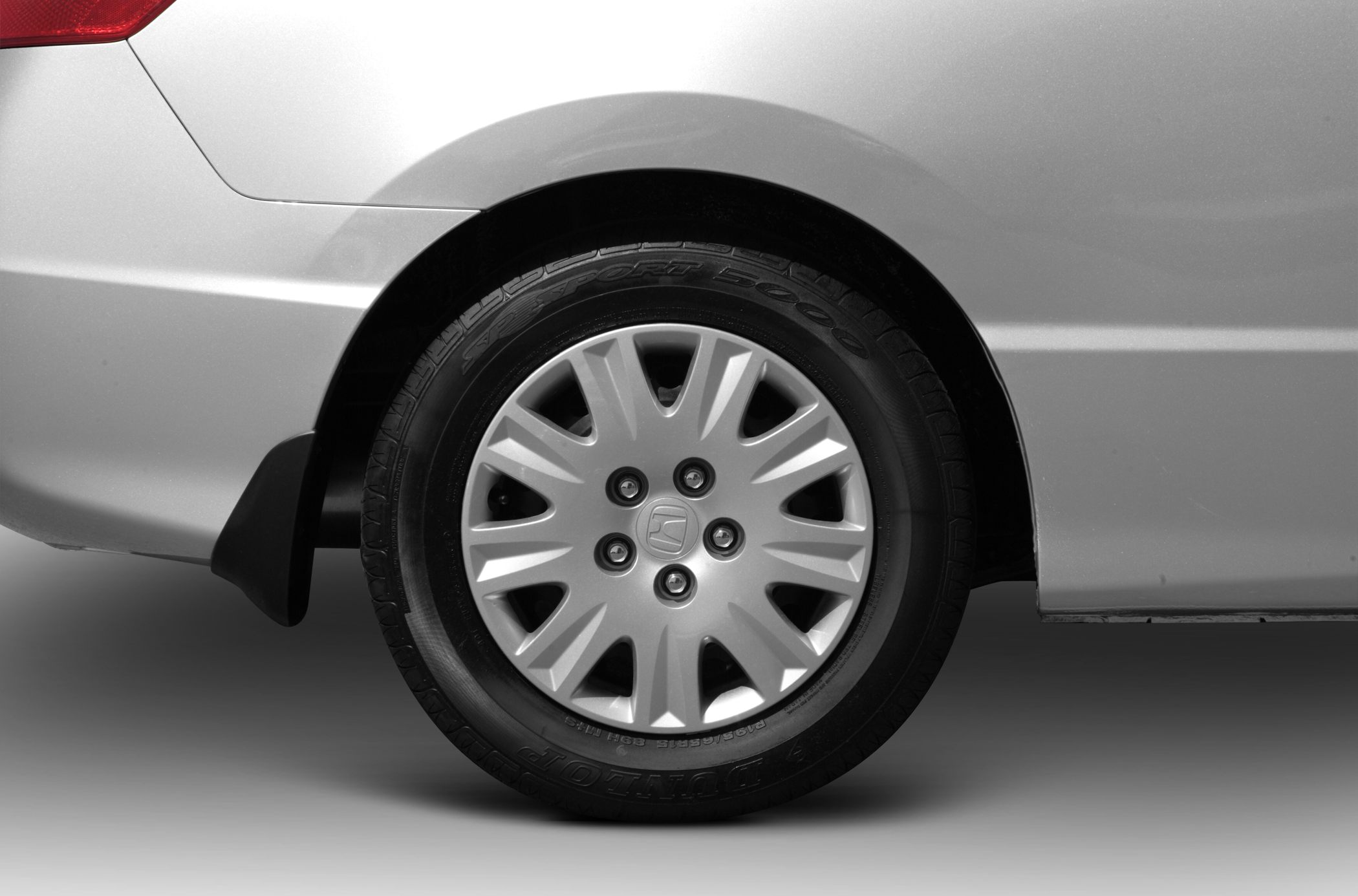 Close-up of rear wheel with hubcap and mudflap on silver car body.