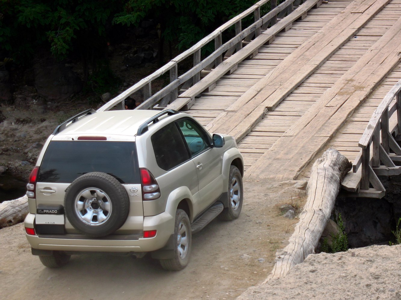 Rear view of SUV with spare tire on rugged terrain near wooden bridge