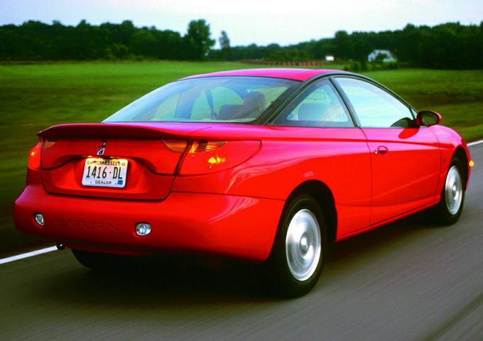 Rear and side view of a red two-door coupe driving on a road